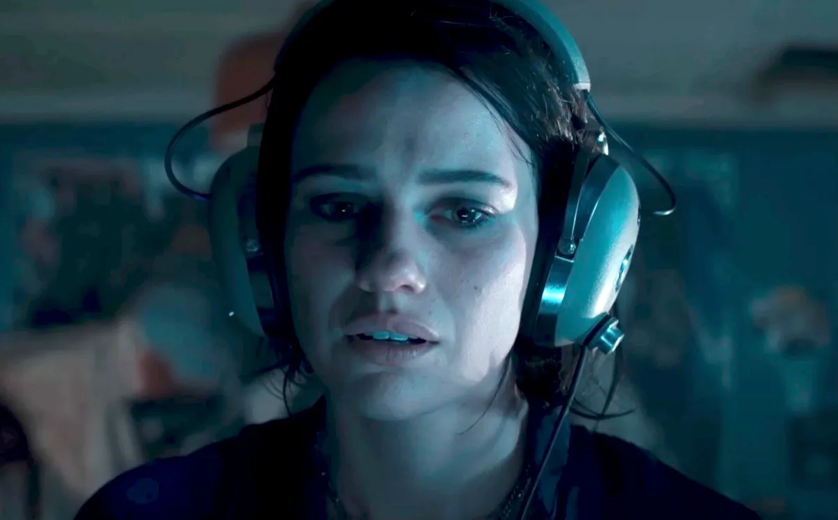 A woman wearing headphones and looking unsettled in Evil Dead Rise.
