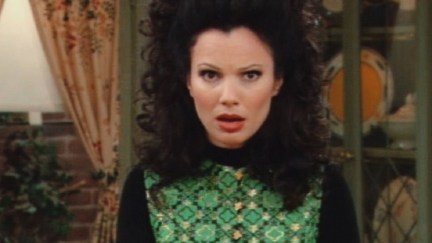 Image of Fran Drescher as Fran Fine in the CBS sitcom, 'The Nanny.' She is standing in the house looking right into the camera with a shocked expression on her face. Fran is a white, Jewish woman with long, curly, black hair worn half up in a ponytail and half down. She's wearing a green patterned top over a long-sleeved black shirt.
