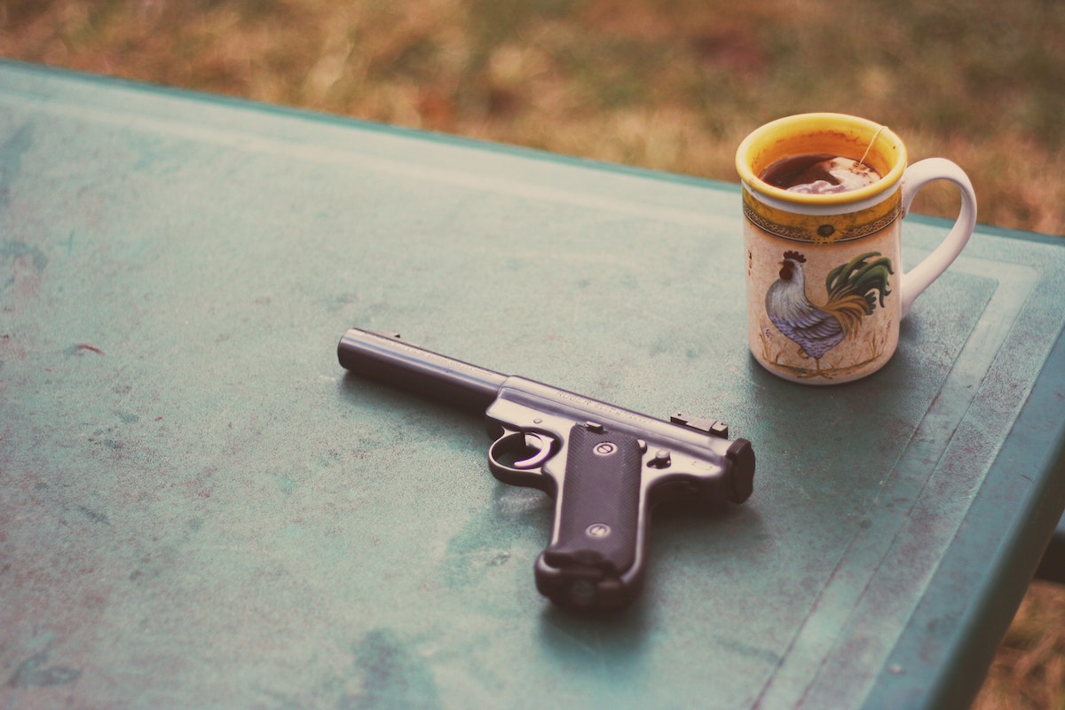 A handgun sits on a blue table with a mug of tea on the corner.