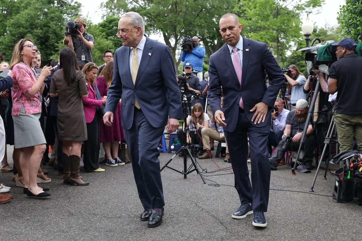 Chuck Schumer and Hakeem Jeffries walk away from a group of reporters gathered outside. Jeffries is wearing dress sneakers.