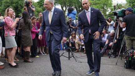 Chuck Schumer and Hakeem Jeffries walk away from a group of reporters gathered outside. Jeffries is wearing dress sneakers.