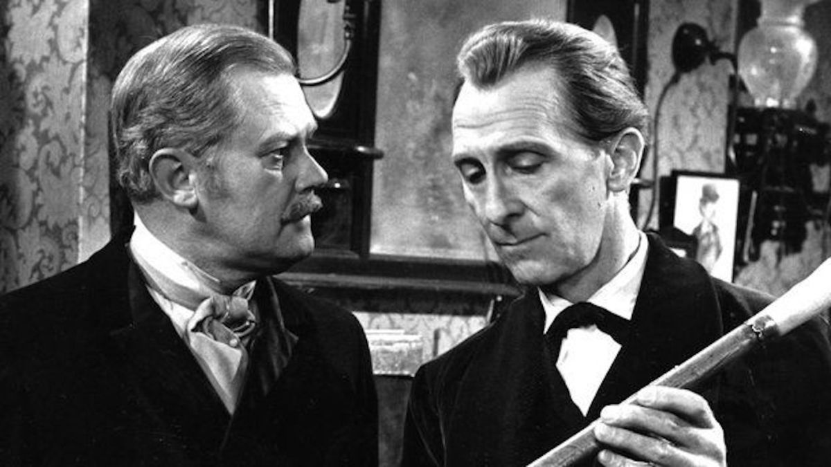 A black and white image of two older white men in suits looking at each other. One is holding a cane.