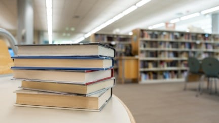 Stack of books on table against bookshelves at a library