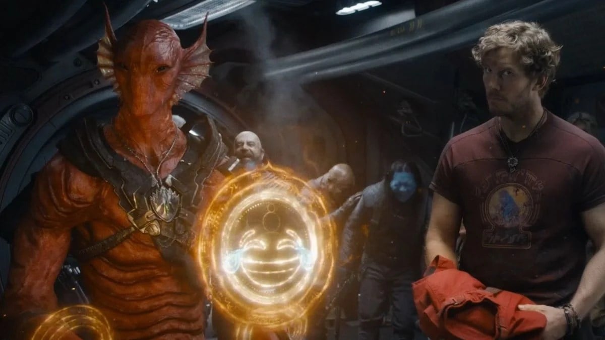 A red alien with fins on either side of his head uses golden magic to create a happy face emoji. Star-Lord looks on, unimpressed.