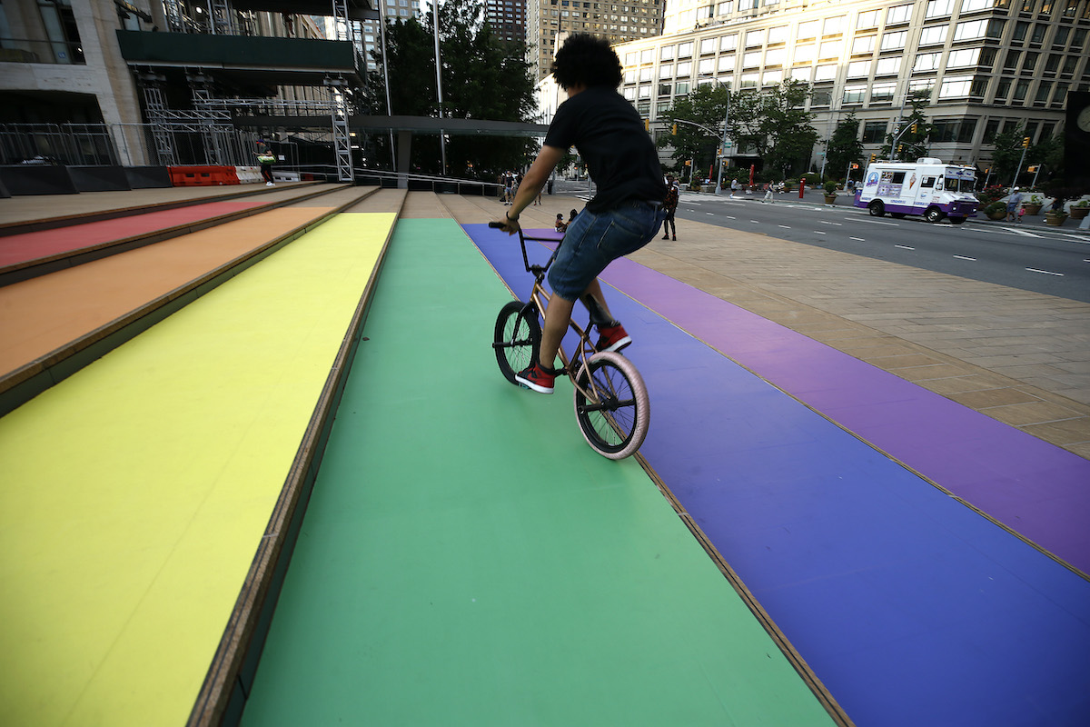 A young person rides a bicycle up a set of steps painted in rainbow colors..