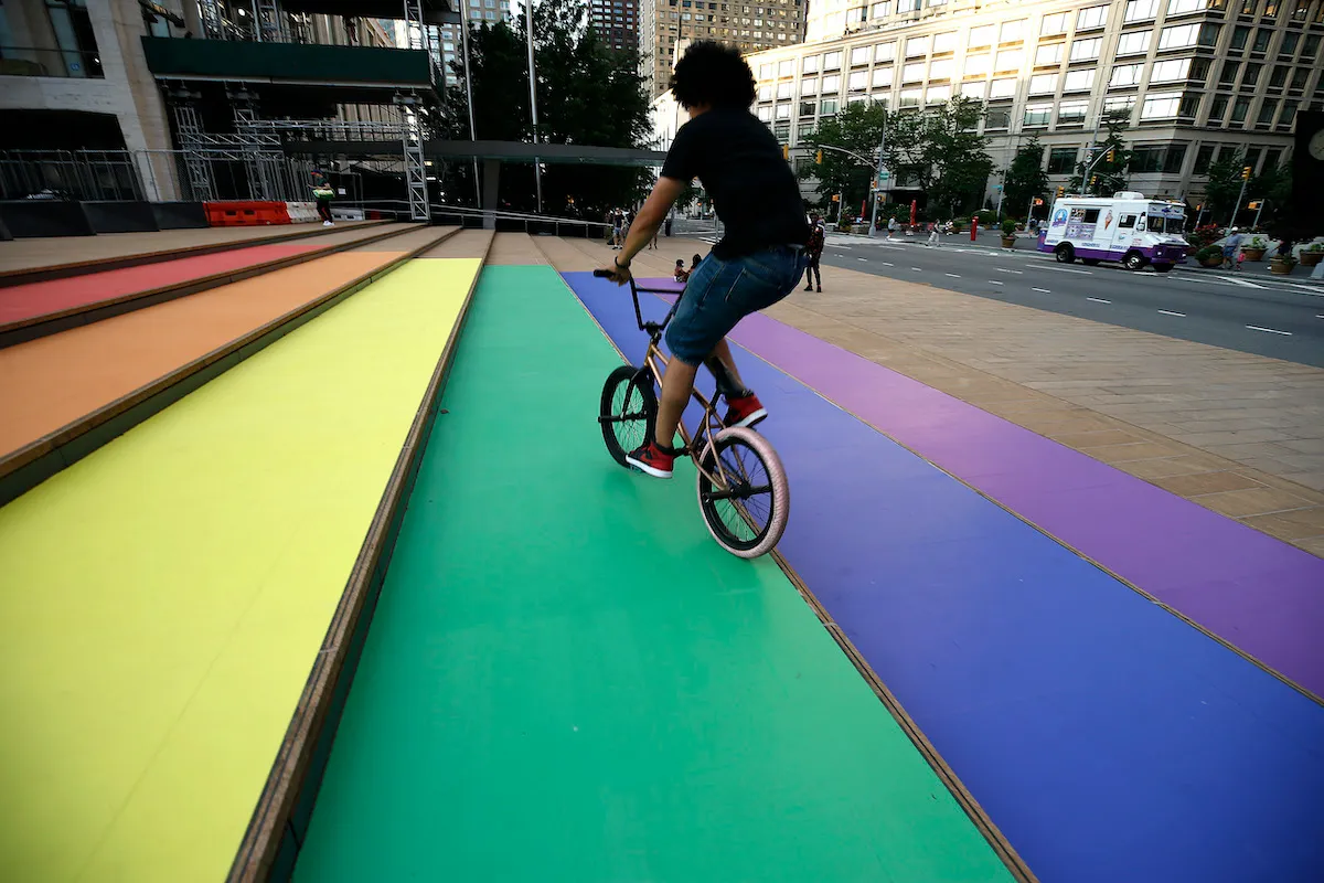 A young person rides a bicycle up a set of steps painted in rainbow colors..