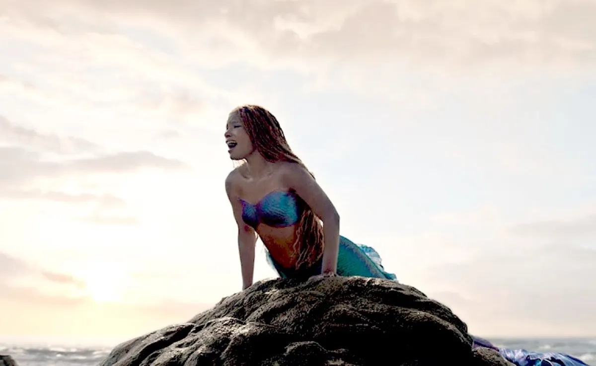 Halle Bailey's Ariel sings atop a rock in the ocean in the live-action The Little Mermaid.