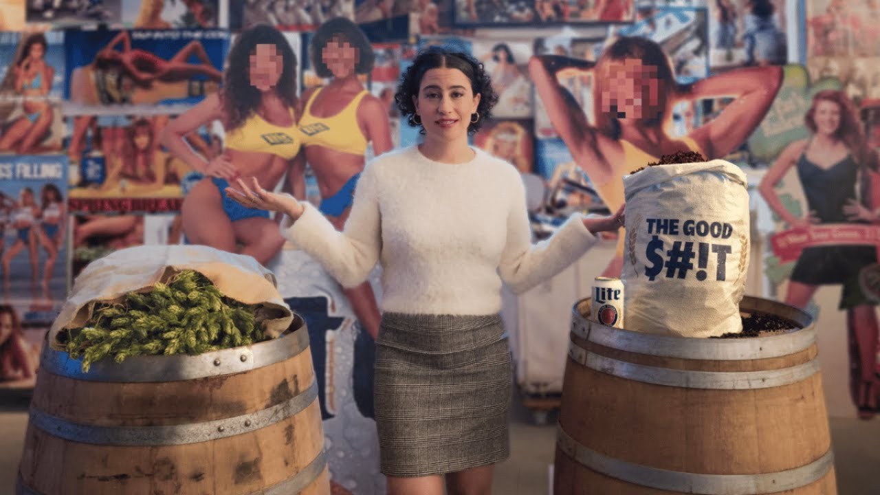 A young woman (Ilana Glazer) walks through a room filled with beer paraphernalia.