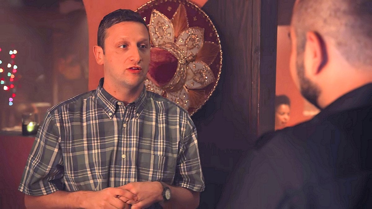 Tim Robinson talks to a man wearing black, with a sombrero hanging on the wall behind him in 'I Think You Should Leave'
