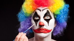 A woman applying make up to her face for her clown costume.