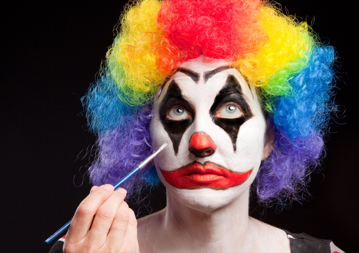 A woman applying make up to her face for her clown costume.