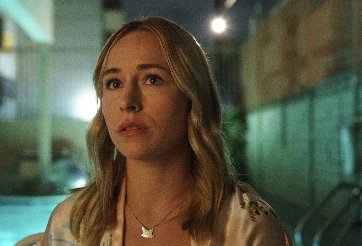 Sally looks up pensively, standing on a street at night.