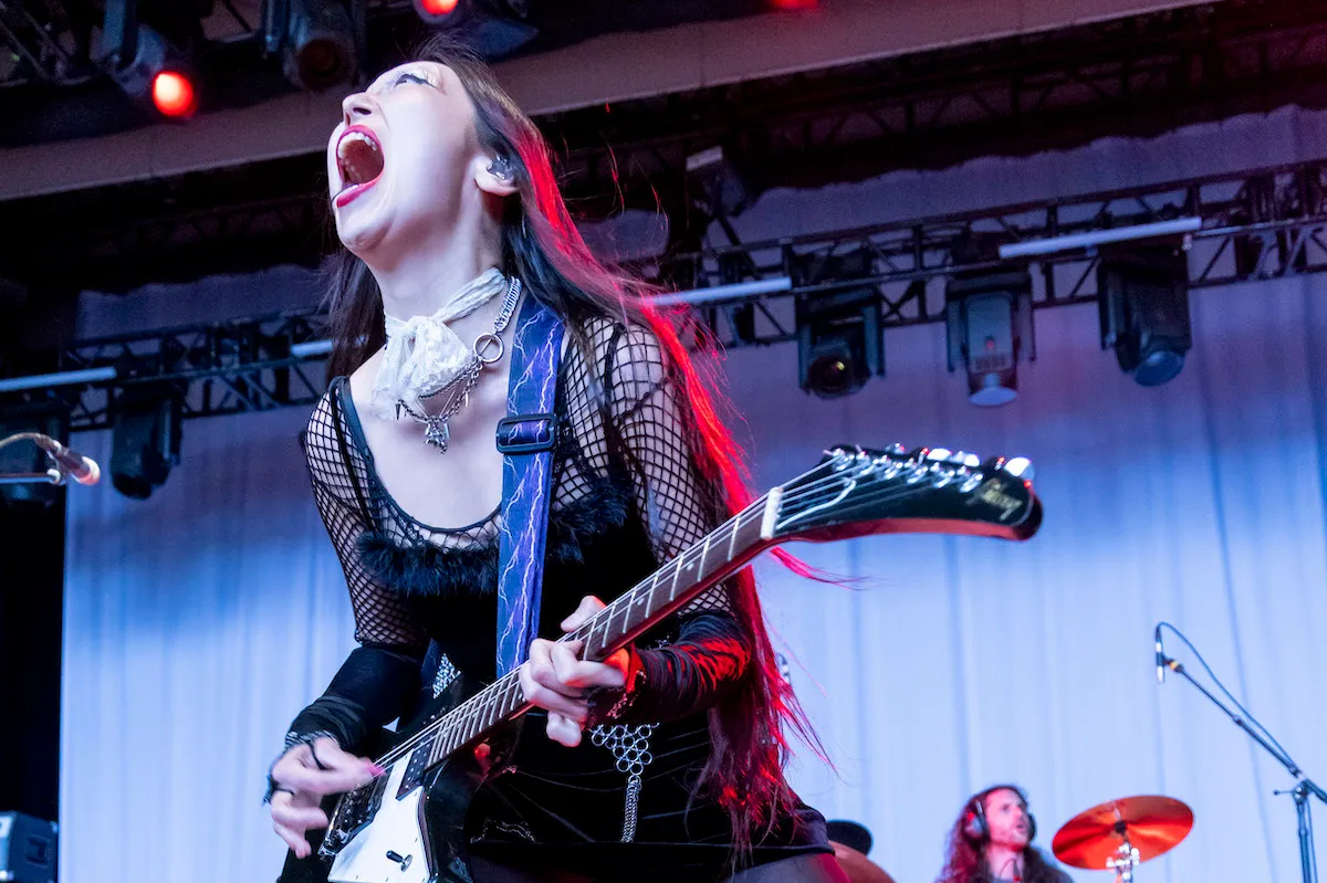 Sasami (an Asian female musician) screams into a microphone on stage while playing electric guitar.