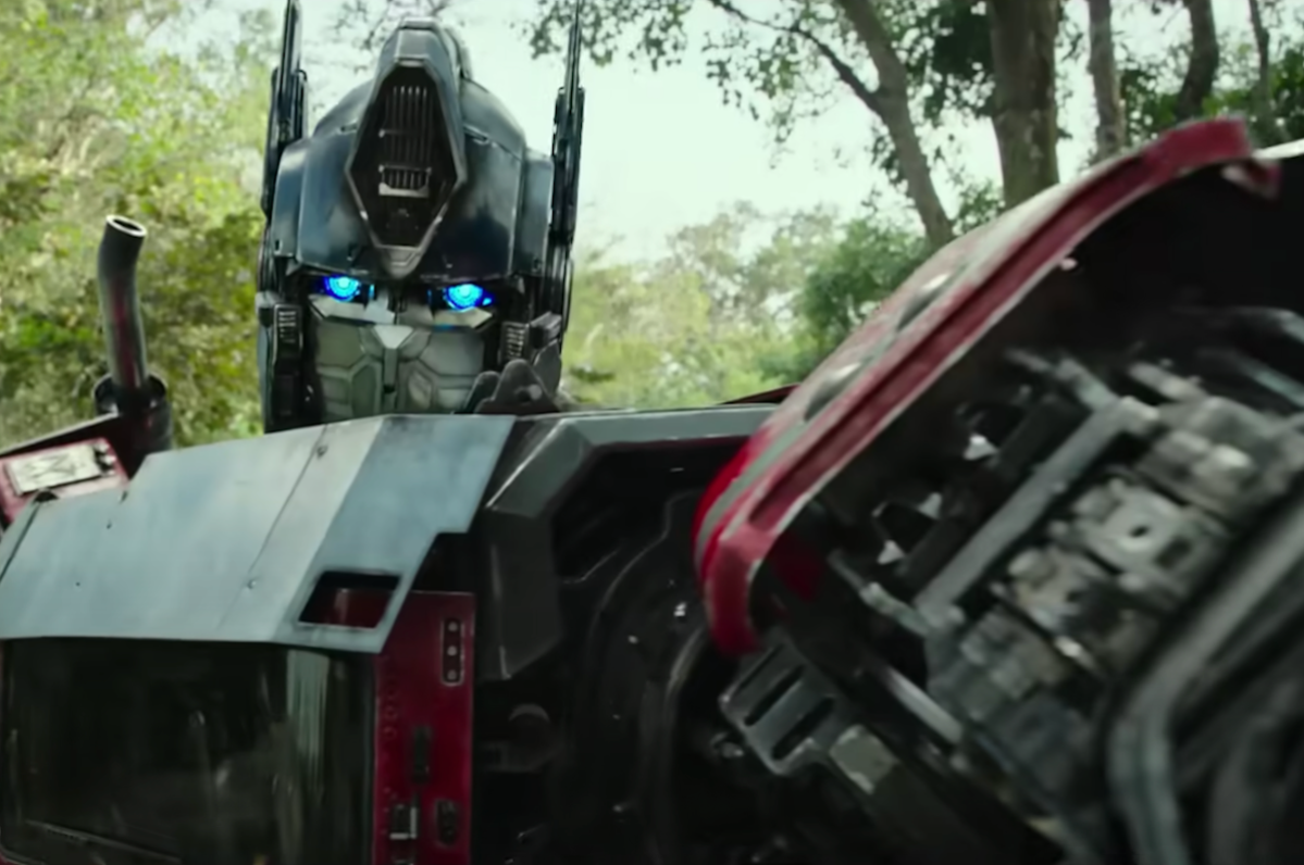 A transformer robot looks right at the camera, holding his arm up and out.