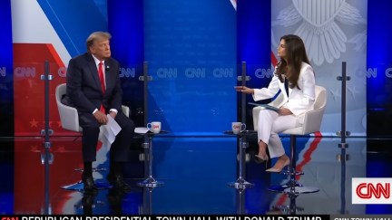 Kaitlan Collins wears a white suit while interviewing Donald Trump on a stage.