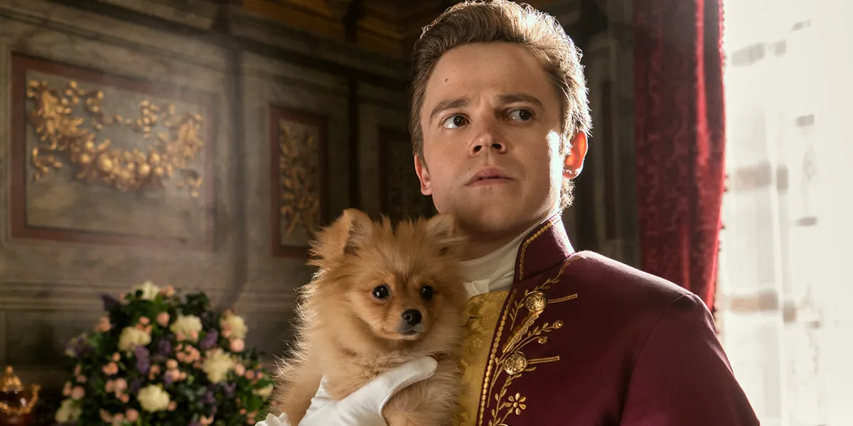 Sam Clemmett as young Brimsley in Queen Charlotte: A Bridgerton Story holding a small Pomeranian dog