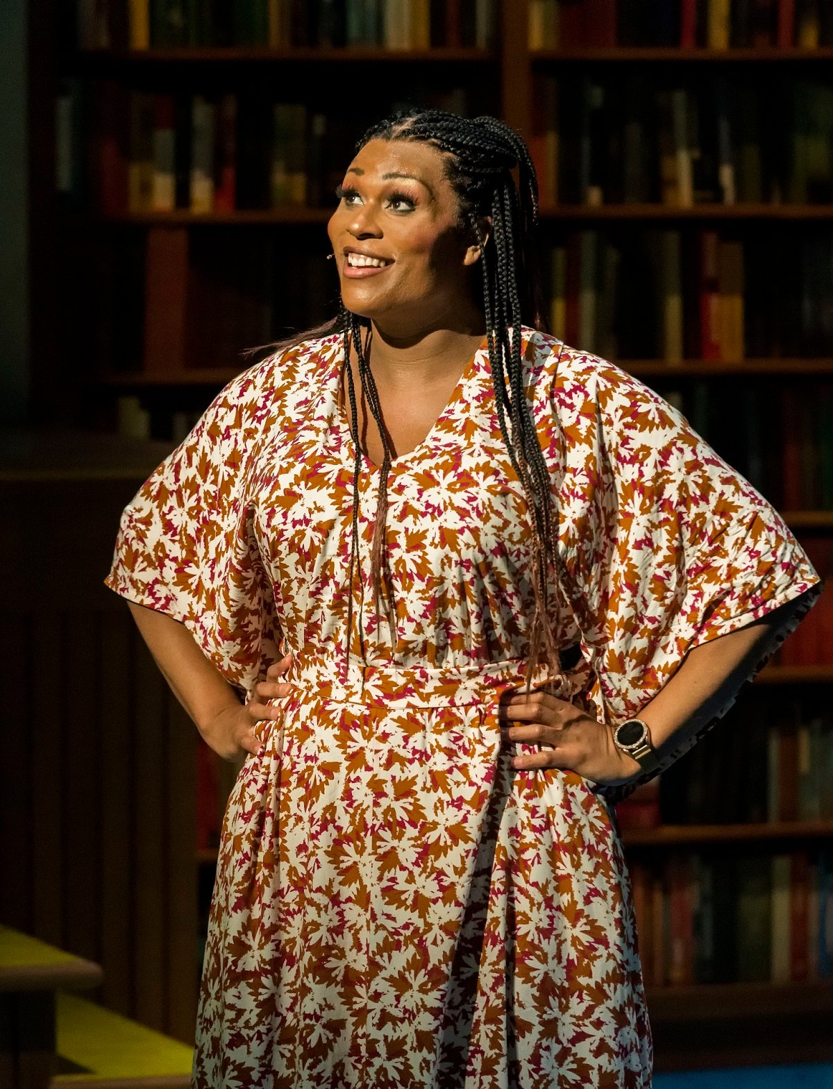 Image of Peppermint as Davina in 'A Transparent Musical' at the Mark Taper Forum in L.A. She is a tall Black woman with long braids standing with her hands on her hips and smiling, wearing a brown and white leaf-patterned dress)