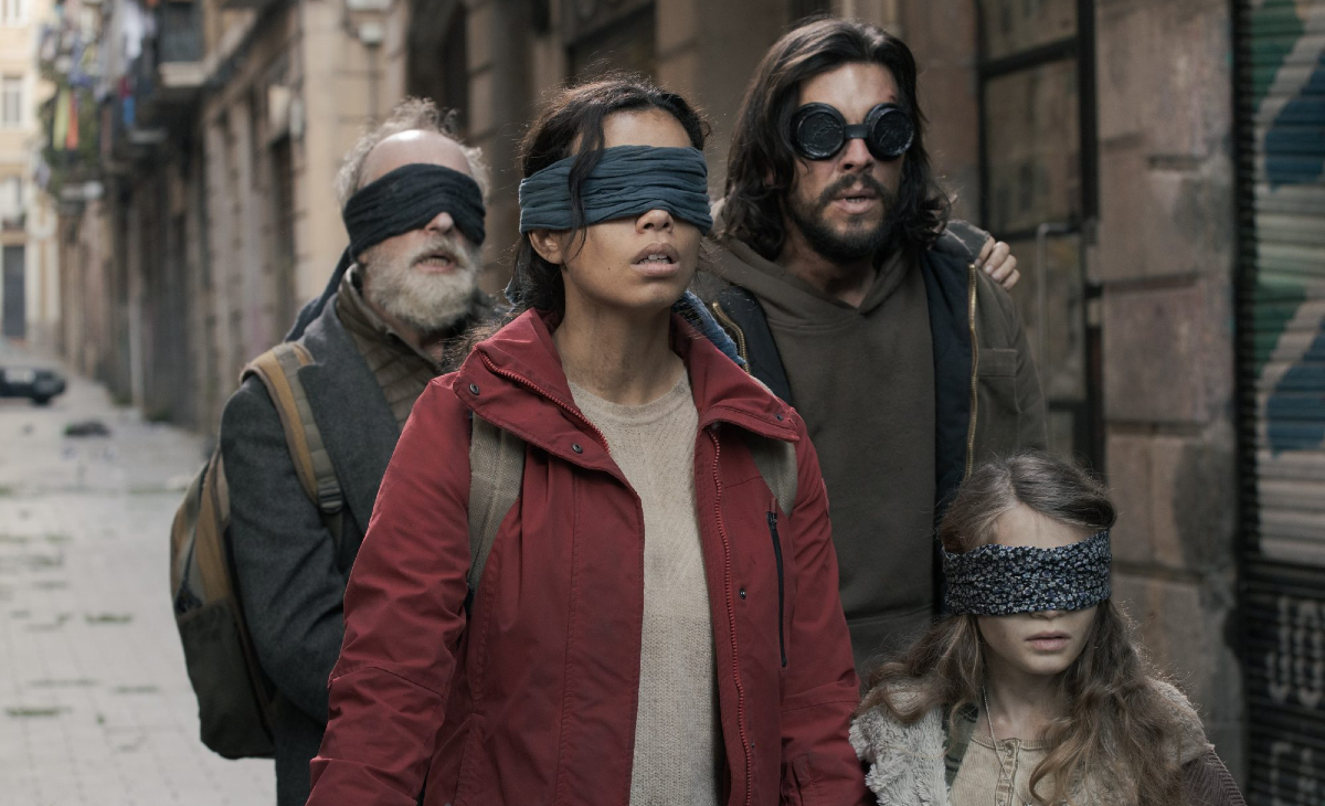 People walk down a city sidewalk with blindfolds covering their eyes in 'Bird Box Barcelona'