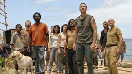 The whole cast of the first season of 'Lost' in a scene from the show. They are all facing the same direction and looking up at something as they stand on the beach.