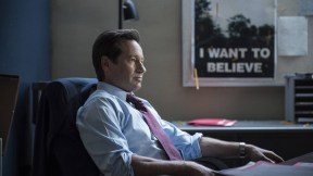 Fox Mulder (David Duchovny) sits at his desk, a poster featuring a flying saucer and the caption 