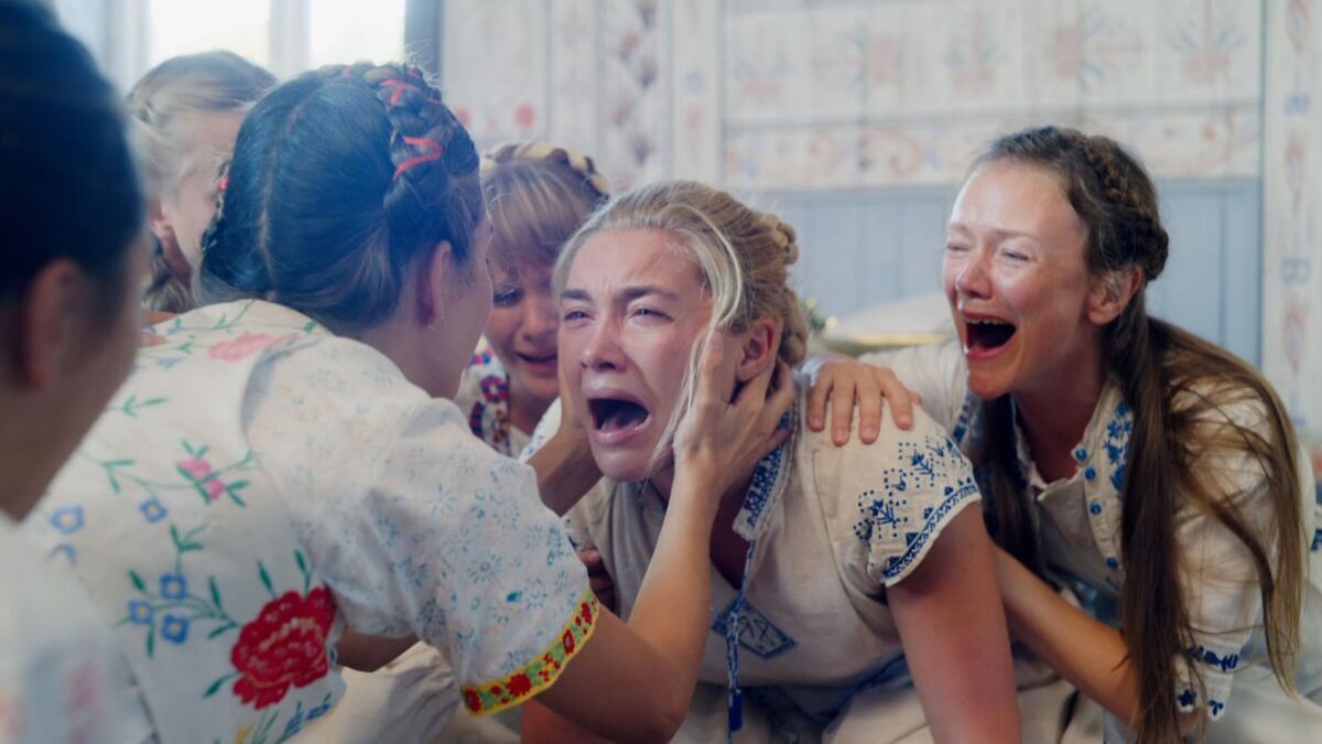 Dani (Florence Pugh) sobs while women in folk dress scream along and comfort her in 'Midsommar'