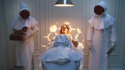 A woman lies in a hospital bed, screaming in fear, with a honeycomb pattern shining on her. Two people dressed as beekeepers stand on either side of her.