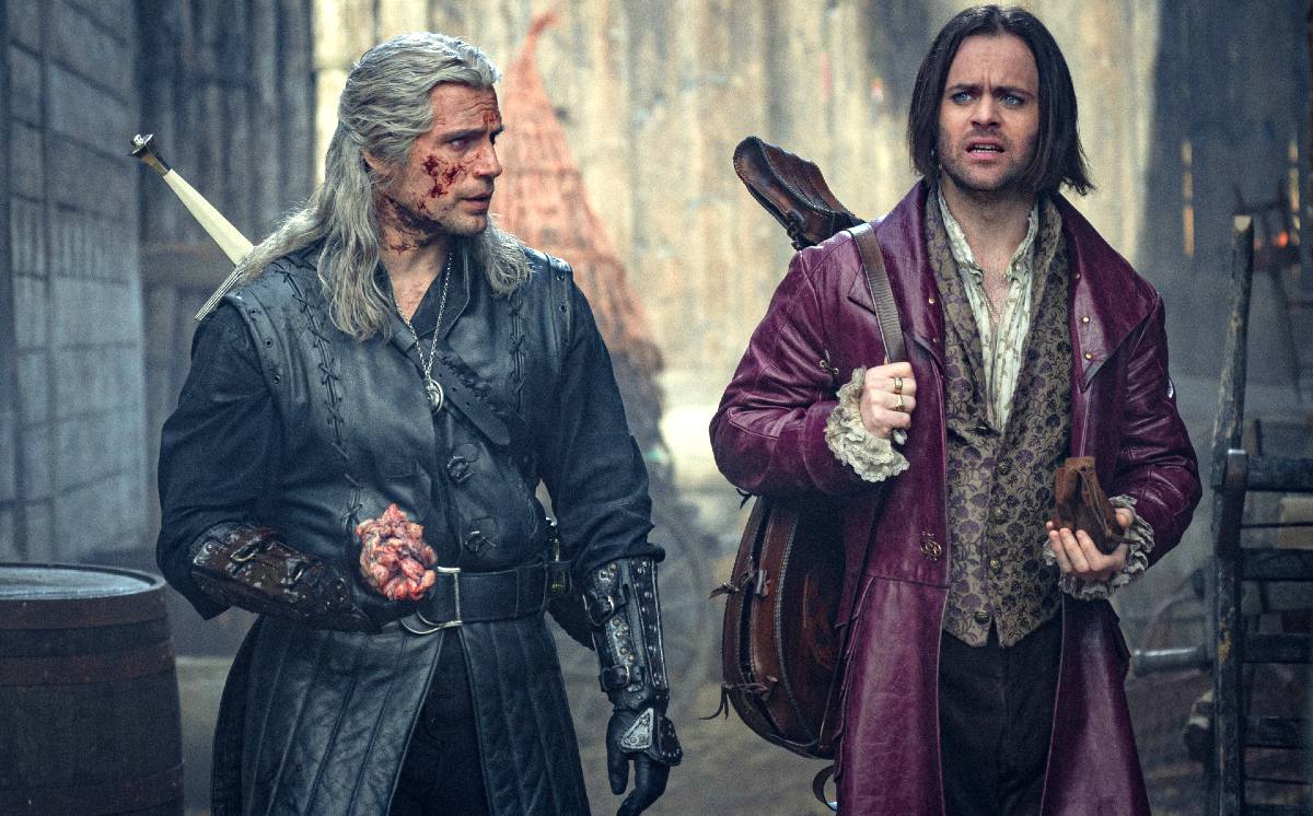 Geralt and Jaskier walk down a back alley in season 3 of The Witcher.