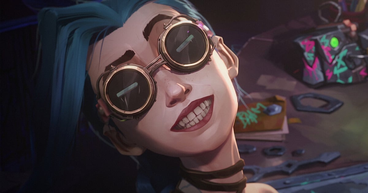 Image of Jinx from Netflix's animated series, 'Arcane.' Jinx is a white teenage girl with long blue hair. We see her from the shoulders up as she looks at us while wearing steampunk goggles and grinning maniacally.