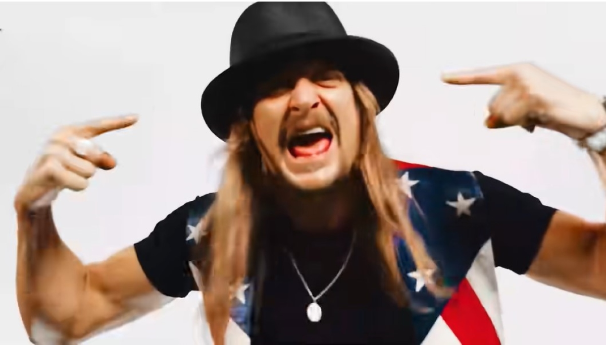 Kid Rock in the music video for "We the People." He's wearing a flag shirt and pointing at his head.