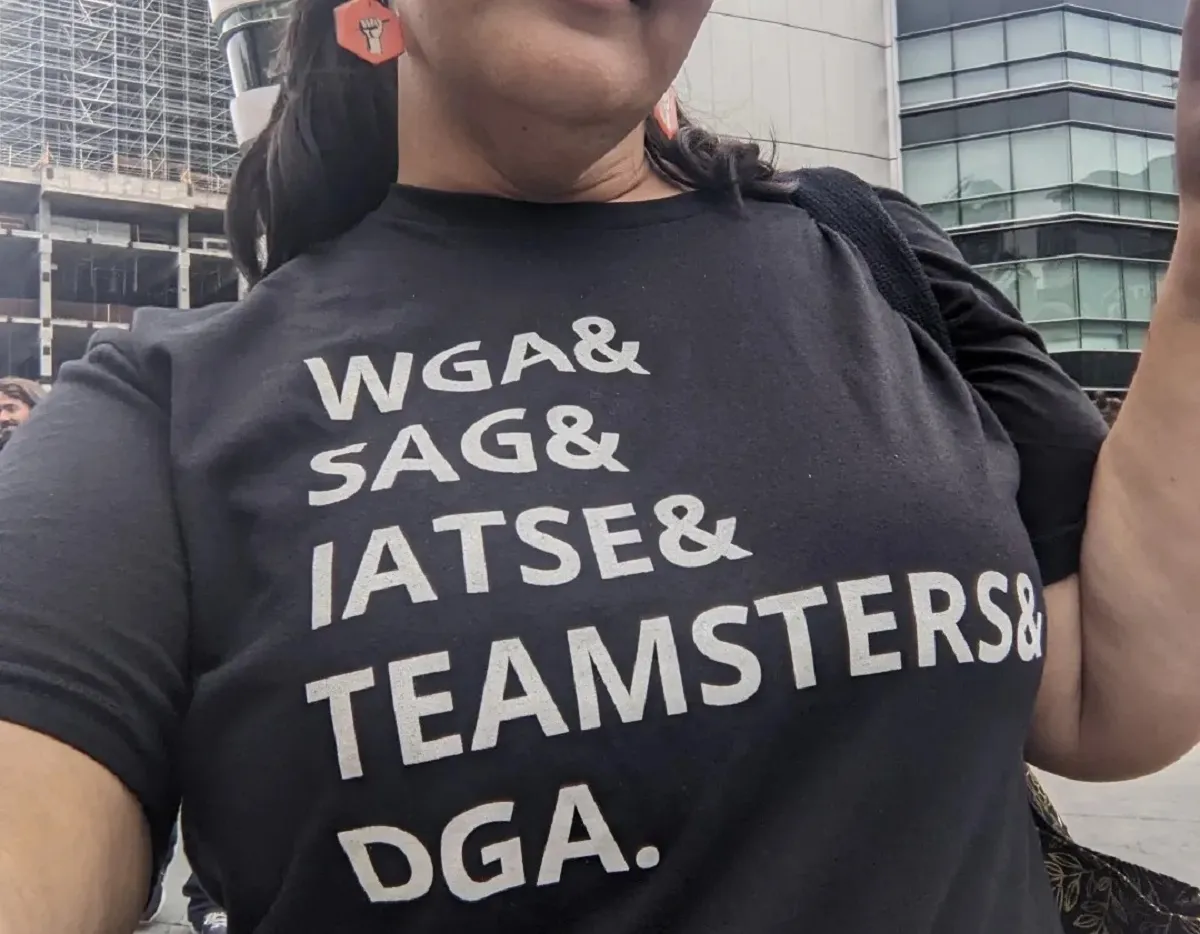 Square image of Teresa Jusino (a brown Latina with long, black hair in pigtails) from the nose down showing off her t-shirt. The t-shirt is black and reads "WGA & SAG & IATSE & TEAMSTERS & DGA."