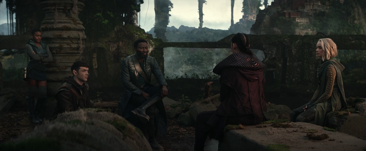 Uhura (Celia Rose Gooding), Spock (Ethan Peck), M'Benga (Babs Olusanmokun), La'an (Christine Chong), and Chapel (Jess Bush) in a scene from 'Star Trek: Strange New Worlds' on Paramount+. They are sitting in a circle having a conversation among ruins on a planet and wearing civilian clothes.