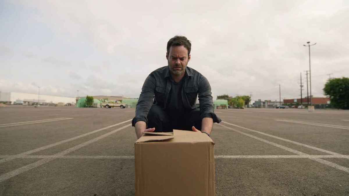 Barry cringes as he picks up a large cardboard box in a parking lot.