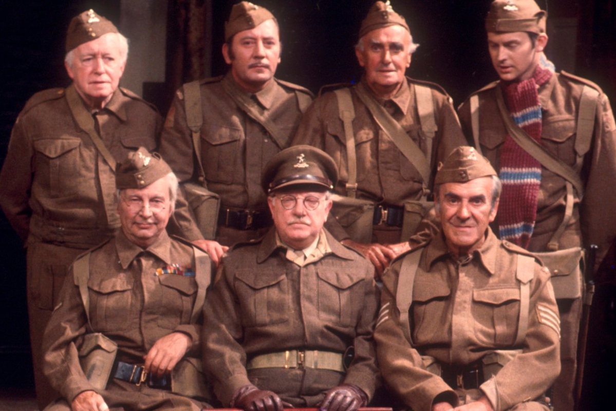 Cast photo from Dad's Army; Left to right, Arnold Ridley, James Beck, John Laurie, Ian Lavendar, Clive Dunn, Arthur Lowe, and John Le Mesurier. A group of white men of varying ages in British army uniforms.