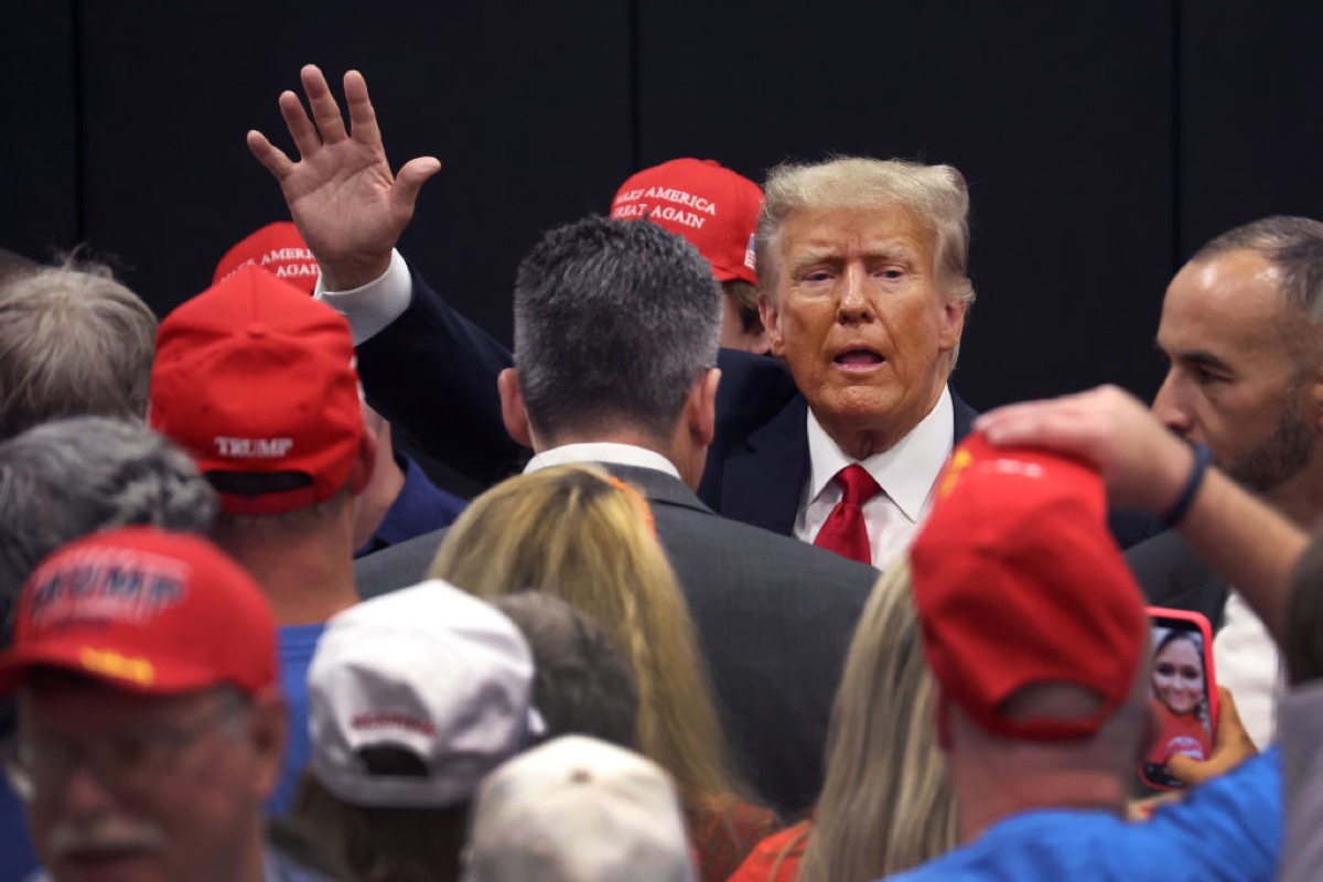 Donald Trump waves to the camera in the midst of a crowd of his supporters.
