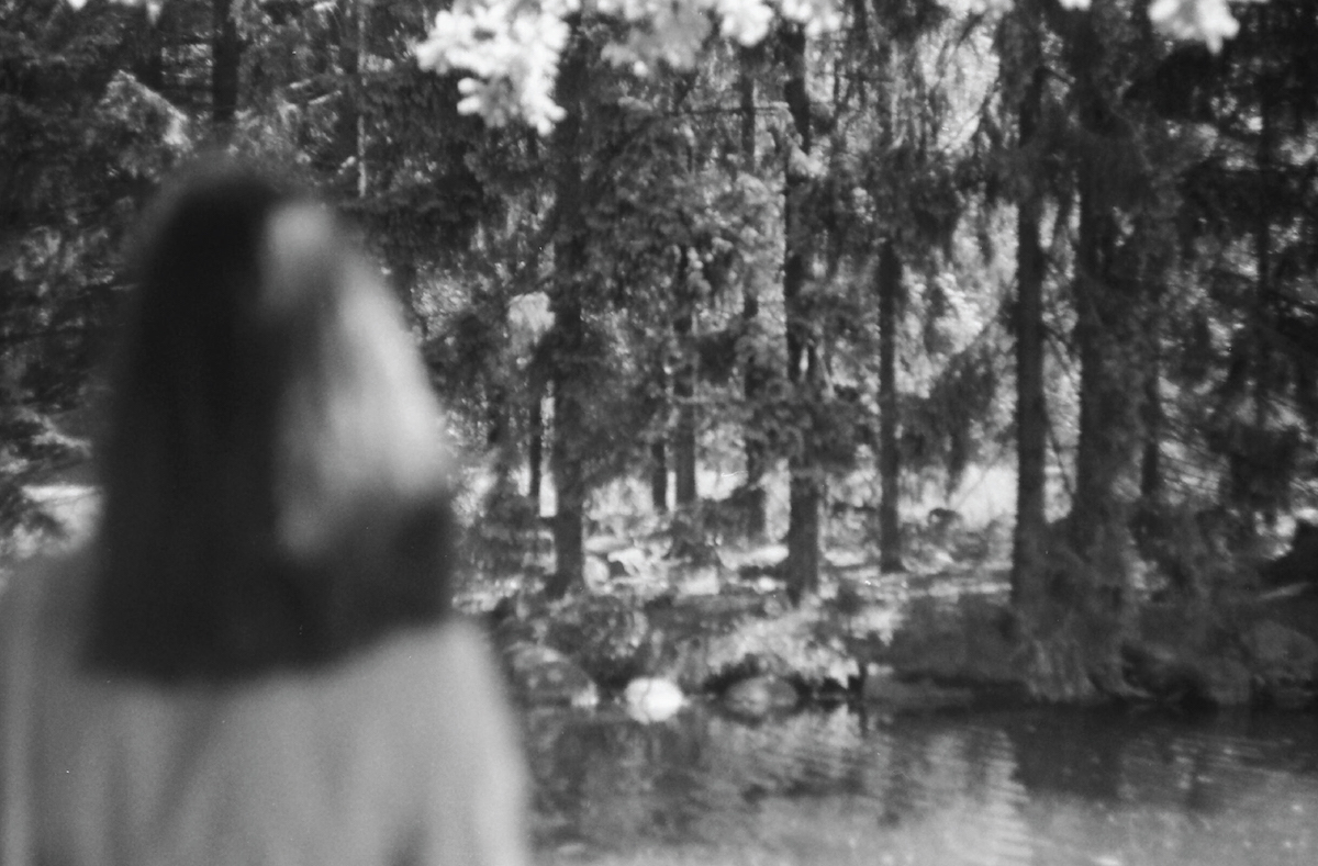 A black and white photo of the back of a woman's head, with a forest beyond her.