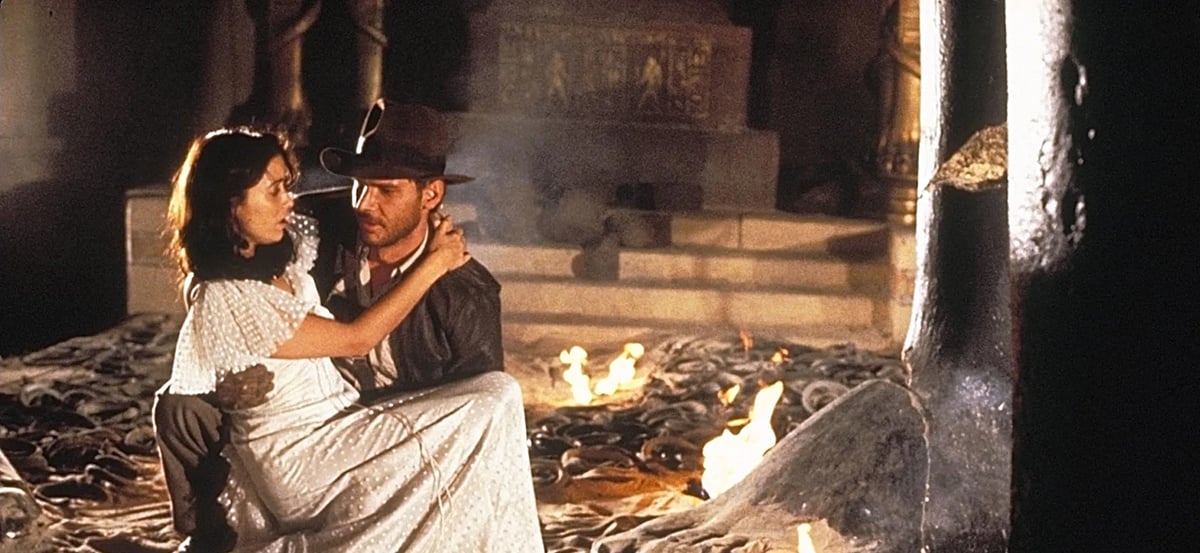 A white man carries a white woman in a white gown out of a cave in "Raiders of the Lost Ark"
