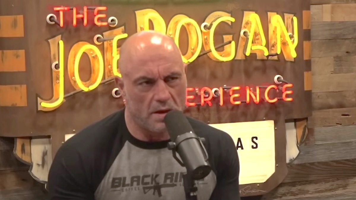Joe Rogan records an episode of his podcast, speaking into a microphone and scowling.