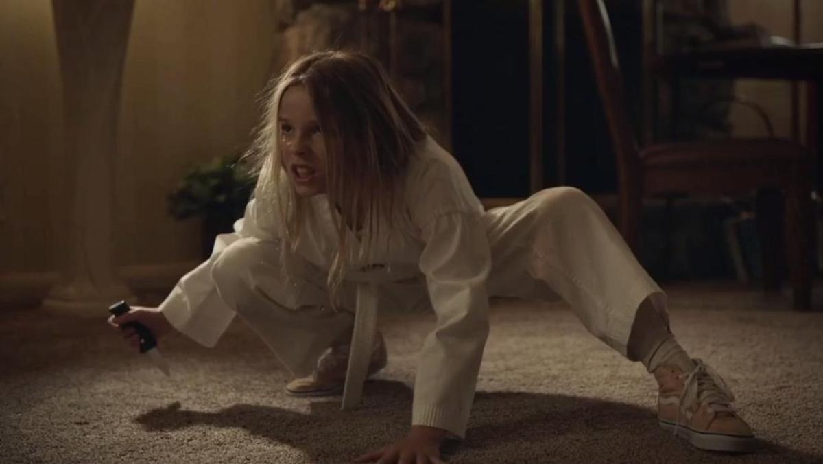 Lily, wearing a karate uniform, squats on the carpet holding a knife.