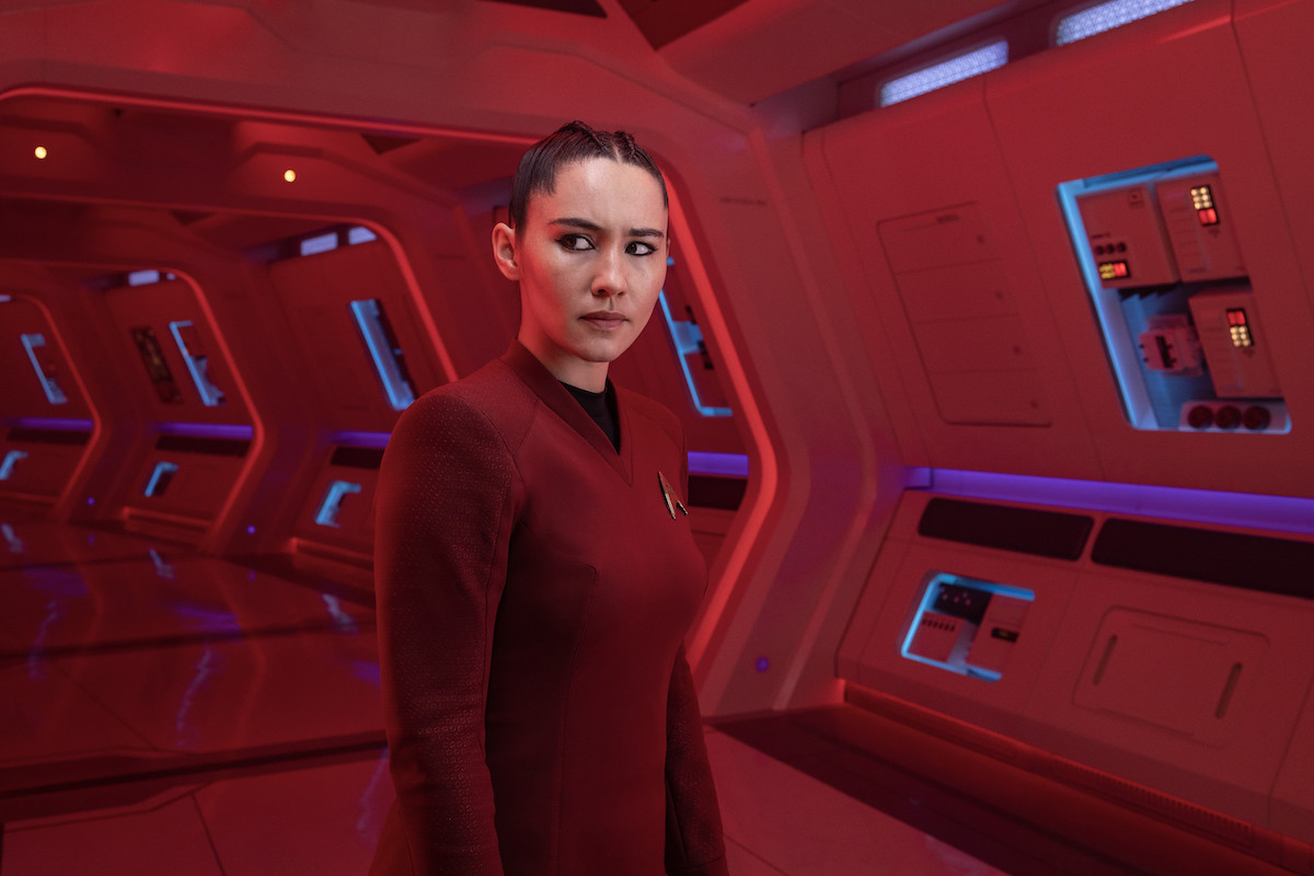 La'an stands in a red hallway on the Enterprise, looking at something off camera.