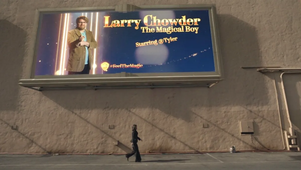 Someone walks under a huge billboard that says "Larry Chowder, the Magical Boy" and shows a man in a tan suit.