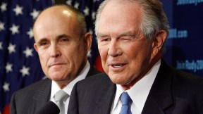 Pat Robertson speaking at microphone while Rudy Giuliani watches.