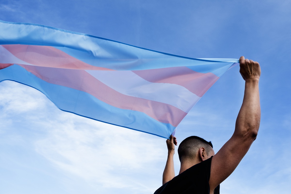 A person holding a transgender pride flag that flows behind them.