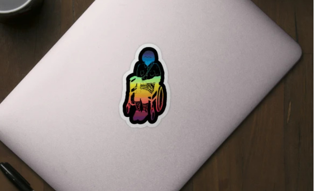 A sticker on a silver laptop featuring a black and white drawing of a femme presenting wheelchair user over a rainbow background.