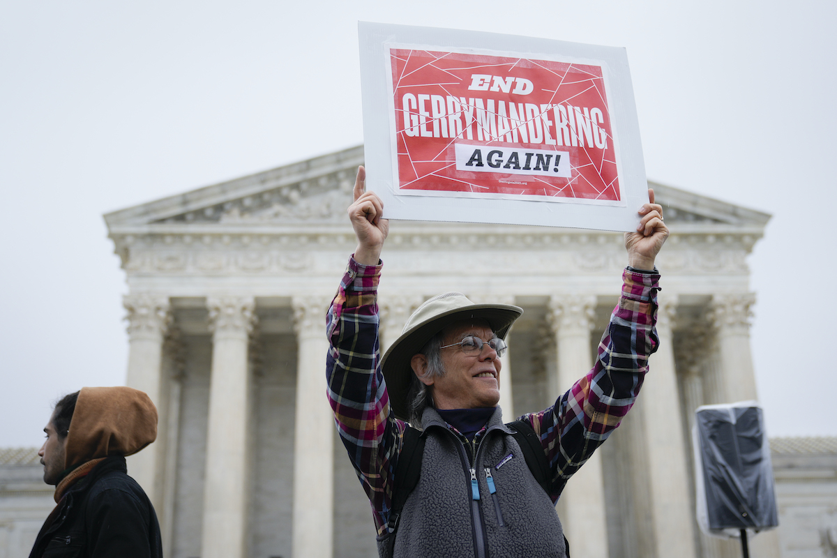 A voting rights activist stands in from of the Supreme Court holding a sign reading "End gerrymandering again"
