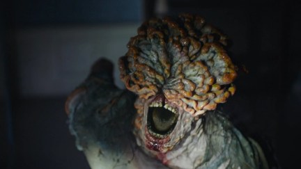 Close-up of a live-action clicker from HBO's 'The Last of Us.' It's leaning forward with its mouth open. Fungal plates have burst out of its face and they're covering its head.