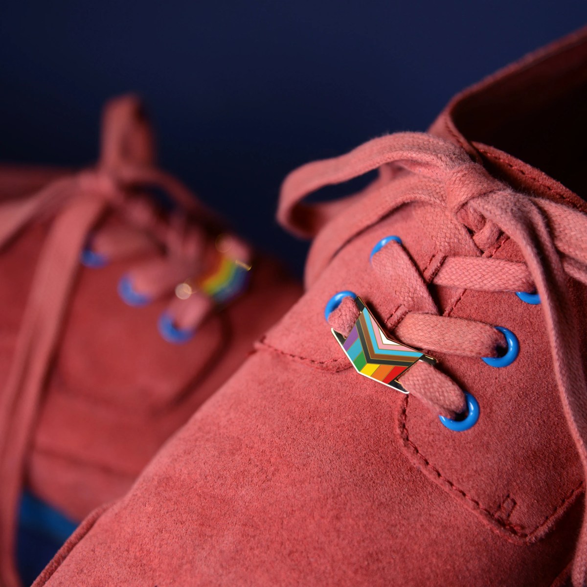 The Pin Prick's Progress Pride Shoe Locks; pink suede shoes with a progress pride enamel shoelaces lock on the laces.