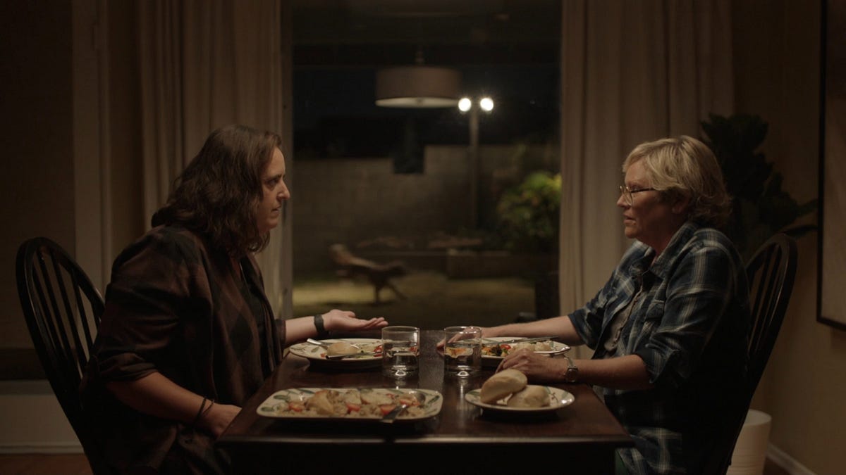 Two women sit at a kitchen table, arguing.