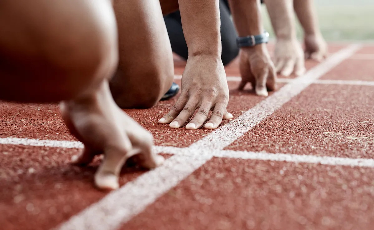 Close up of the hands of runners, crouching at the starting block before a race.