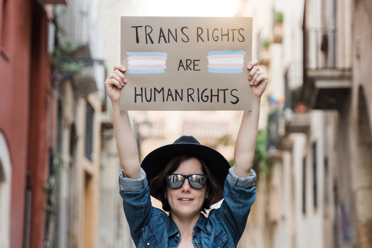 Person in a city holding up a sign that reads "trans rights are human rights."
