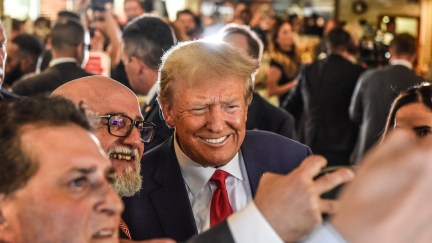 Donald Trump stands in a crowd of supporters, smiling for selfies.